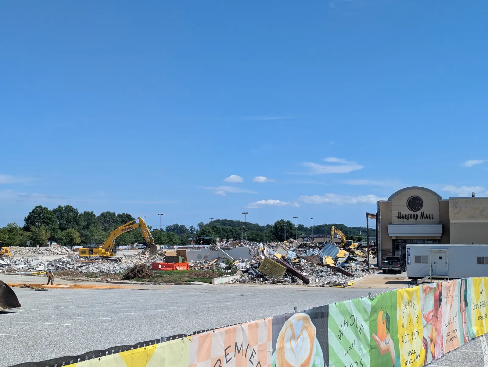 Excavators working through twisted metal and rubble beside the retained Harford Mall entrance